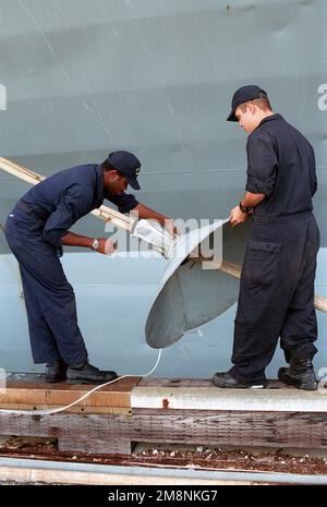 Zwei Matrosen der US Navy (USN), die der USS BLUE RIDGE (LCC-19) zugewiesen sind, befestigen an den Anlegestellen Rattenwächter, während das Schiff am Sierra Pier, Guam, anlegt, während der TANDEM-SCHUB 99 ausgeübt wird. Betrifft Operation/Serie: TANDEM-SCHUBKRAFT-Basis 99: Sierra Pier Staat: Guam (GU) Land: Nördliche Marianen (MNP) Stockfoto