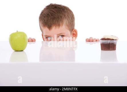 Apfel, Kuchen und Auswahl mit einem Jungen, der im Studio auf weißem Hintergrund zwischen Süßigkeiten oder Gesundheit entscheidet. Essen, Obst und Entscheidung bei einem männlichen Kind Stockfoto