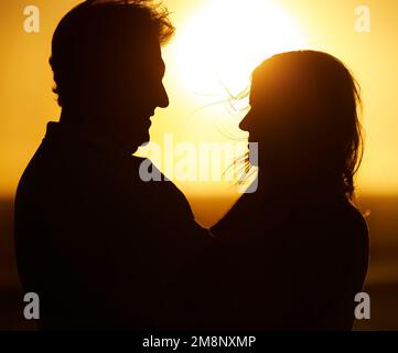 Reifes Paar, das sich am Strand umarmt. Silhouette eines erwachsenen Paares, das am Strand liebevoll ist. Seniorenpaar, das sich im Urlaub am Meer anfreundet. Fürsorglich Stockfoto