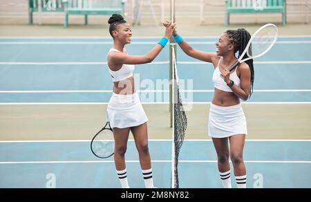 Zwei professionelle Tennisspieler, die nach einem Spiel lachen. Junge afroamerikanische Mädchen, High Five am Tennisnetz auf dem Platz. Fröhliche Tennisspieler Stockfoto