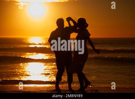 Silhouette liebevolles Seniorenpaar teilt einen intimen Moment am Strand. Beleuchteter glücklicher Ehemann und Ehefrau genießen einen Sommertag am Meer. Sie Stockfoto