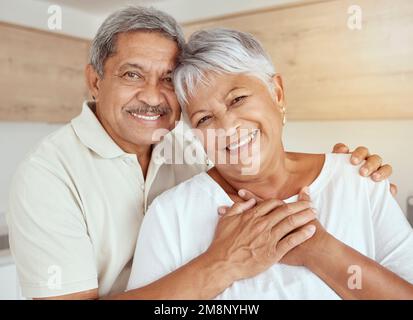 Porträt eines gemischten Seniorenpaares, das sich morgens zu Hause umarmt. Lächelnder älterer Ehemann und Ehefrau, die sich in der Küche halten und umarmen. Alles gute zum Ruhestand Stockfoto