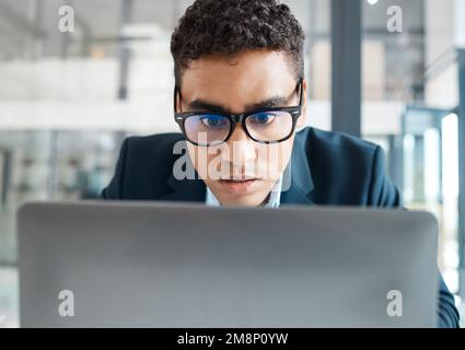 Ein seriöser Geschäftsmann aus gemischten Rassen, der alleine an einem Notebook arbeitet. Das Gesicht eines hispanischen Geschäftsmanns, der eine E-Mail auf einem Laptop liest Stockfoto