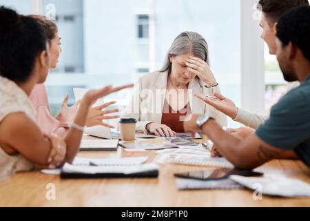 Eine Gruppe von Geschäftsleuten, die sich in einem Konferenzraum bei der Arbeit treffen. Gestresste, reife, weiße Geschäftsfrau, die während ihrer Zeit an Kopfschmerzen leidet Stockfoto