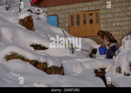 Srinagar, Indien. 14. Januar 2023. Eine Frau hält einen Eimer Wasser auf den Hügel, nach einem frischen Schneefall am Stadtrand von Srinagar. Das Wetter verbesserte sich im Kaschmir-Tal nach Tagen mit moderatem bis starkem Schneefall und Regen. In der Zwischenzeit wurden am Samstag Lawinen im Bezirk Bandipora und im Bahnhof Sonamarg gemeldet, bei denen es in den letzten Tagen zu moderaten bis schweren Schneefällen kam. Dies ist der zweite Vorfall, der in den letzten zwei Tagen in der beliebten Hill Station gemeldet wurde. Zwei Arbeiter starben am Donnerstag, als eine Lawine die Baustelle einer Baufirma in Sonamarg traf. Kredit: SOPA Stockfoto