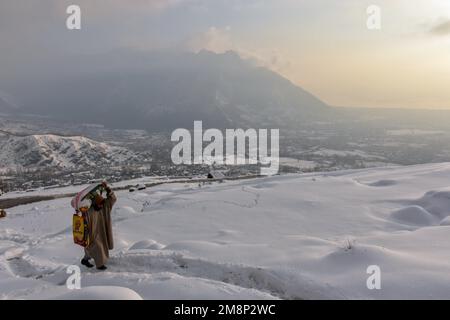 Srinagar, Indien. 14. Januar 2023. Ein Mann trägt eine Tüte mit Essen, während er nach einem frischen Schneefall am Stadtrand von Srinagar den schneebedeckten Hügel entlanggeht. Das Wetter verbesserte sich im Kaschmir-Tal nach Tagen mit moderatem bis starkem Schneefall und Regen. In der Zwischenzeit wurden am Samstag Lawinen im Bezirk Bandipora und im Bahnhof Sonamarg gemeldet, bei denen es in den letzten Tagen zu moderaten bis schweren Schneefällen kam. Dies ist der zweite Vorfall, der in den letzten zwei Tagen in der beliebten Hill Station gemeldet wurde. Zwei Arbeiter starben am Donnerstag, als eine Lawine die Baustelle einer Baufirma in Sonama traf Stockfoto