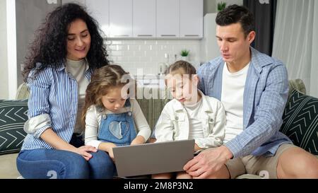 Aufmerksame Eltern sehen aufgeregten Geschwistern beim Spielen auf einem Laptop zu Stockfoto