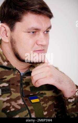 Der ukrainische Soldat lehnte sich an seine Hand und dachte, er schaue nach unten. Er hat einen wunderschönen Bart und eine Uniform mit blauen Augen. Eine Menge Schmerz und Traurigkeit in sich Stockfoto