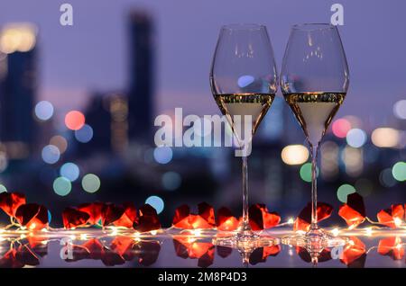 Zwei Gläser Weißwein auf dem Tisch mit einer hellen Paparenfalte mit Herz und einem bunten Bokeh-Licht aus der Stadt für das Valentinstag-Speisekonzept. Stockfoto