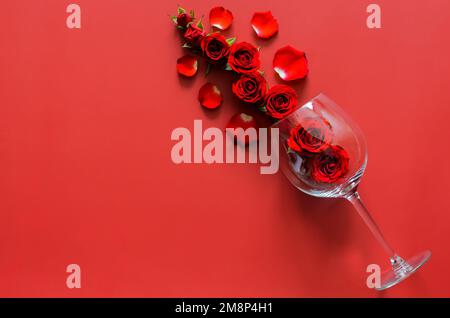 Rote Rosen mit leerem Rotweinglas auf rotem Hintergrund für das Valentinstag-Speisekonzept. Stockfoto