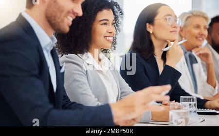 Glückliche junge Geschäftsfrau gemischter Rassen, die während eines Meetings in einem Vorstandssaal zusammen mit ihren Kollegen eine Präsentation anhört. Vielfältige Gruppe von Stockfoto