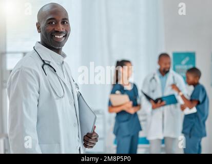 Portrait eines glücklichen, reifen afroamerikanischen männlichen Arztes, der einen Ordner hält, der mit Kollegen in einem Krankenhaus arbeitet. Fachkundiger Arzt lächelt Stockfoto