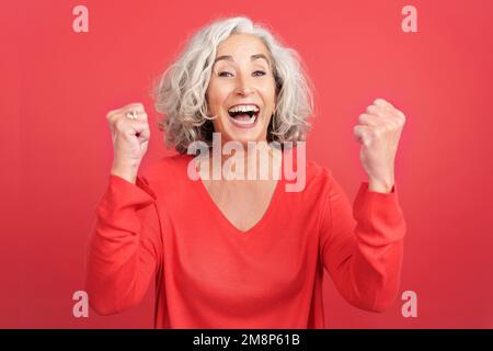 Reife Frau feiert, während sie die Fäuste erhebt Stockfoto