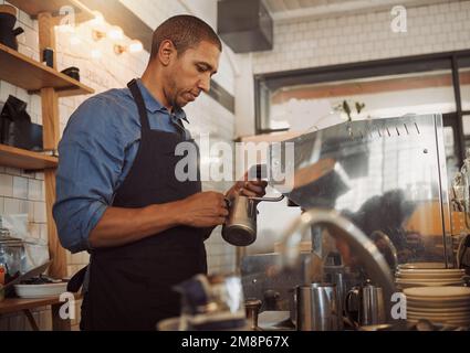 Der Barista schäumt während der Kaffeezubereitung Milch auf. Kaffee-Assistent, der Kaffee für Gäste zubereitet. Fokussierter Barista hält eine Kanne, um Milch aufzuschäumen. Barista Stockfoto