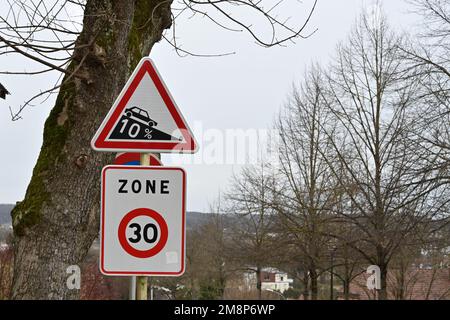 Ein dreieckiges Verkehrszeichen mit roter Umrandung, das auf eine Neigung von 10 % hinabfährt. Stockfoto