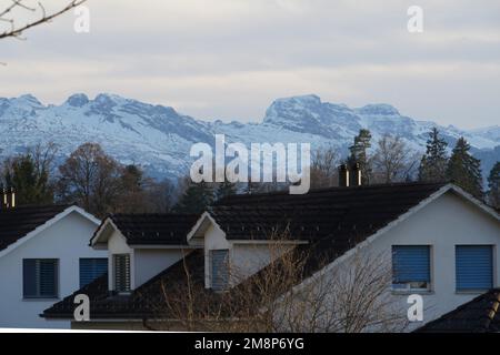 Dächer eines Wohnviertels in einer Schweizer Stadt Hinwil, umgeben von Alpenbergen. Die Berge sind mit Schnee bedeckt. Stockfoto