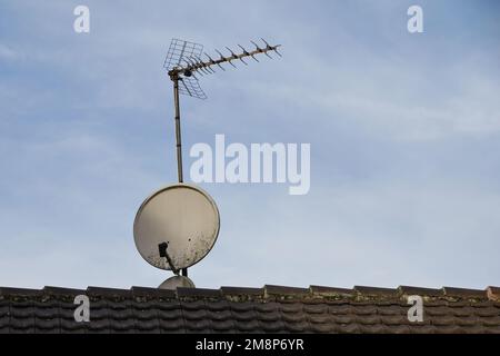 Eine analoge Antenne und eine Satellitenantenne befinden sich auf dem Dach eines gefliesten Dachs. Stockfoto