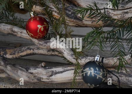 Rote und blaue Weihnachtsbälle mit goldenen Ornamenten sind als saisonale Außendekoration auf Nadelzweigen angeordnet. Stockfoto