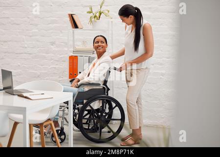 Junge gemischte Geschäftsfrau, die einer Kollegin im Rollstuhl bei der Arbeit in ihr Büro hilft. Hispanischer Geschäftsmann mit Behinderung, dem geholfen wird Stockfoto