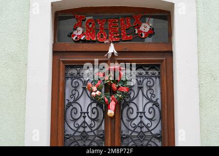 Eine hölzerne Haustür in Frankreich mit Weihnachtsdekoration und einer Inschrift in französischer Sprache mit der Aufschrift Frohe Weihnachten. Stockfoto