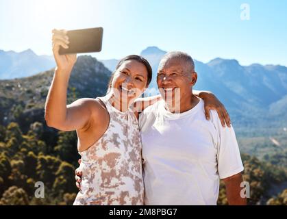Glückliches, reifes Paar, das ein Selfie macht oder Videoanrufe führt, während es im Freien in Sportbekleidung steht. Aktives Seniorenpaar genießt einen gesunden Lebensstil Stockfoto