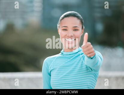 Porträt einer selbstbewussten jungen Frau aus gemischten Rassen, die beim Sport im Freien die Daumen nach oben streckt. Glückliche Sportlerin, die motiviert und bereit für einen ist Stockfoto