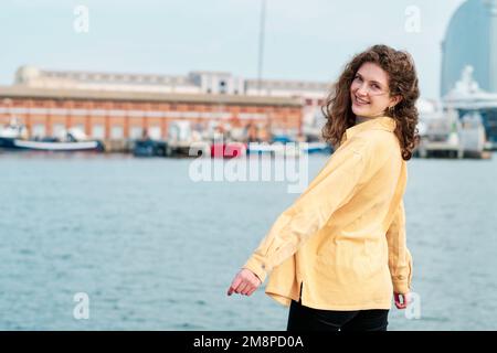 Junge Frau lächelt, während sie sich draußen auf der Meerespromenade posiert. Stockfoto