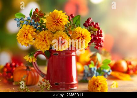 Blumige Stille im Herbst mit wunderschönen gelben Dahlien und Beerenzweigen in altem roten Krug und Kürbissen auf dem Tisch. Herbstfestkonzept. Stockfoto