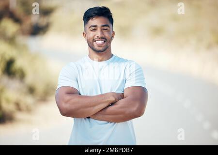 Porträt eines jungen Mannes mit gemischten Rassen, der stolz aussieht, mit gekreuzten Armen auf der Straße, nachdem er draußen trainiert hat. Ein indischer Mann, der lächelt und sich fühlt Stockfoto