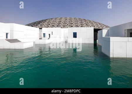 Außenansicht des modernen Gebäudes des Louvre in Abu Dhabi, mit der Gitterkuppel und der weißen Marmorwand, umgeben von Wasser Stockfoto