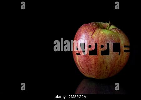 Frischer Apfel mit geschnitzter Inschrift. Apfel mit Wassertropfen auf schwarzem Hintergrund. Stockfoto