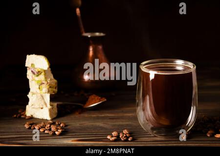 Frischer schwarzer Kaffee, der in der richtigen Enghalszeder gebrüht wird. Türkische Süßigkeiten. Türkische Halva mit Pistazien. Verstreute Kaffeebohnen Stockfoto