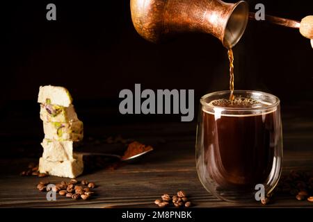 Frischer schwarzer Kaffee, der in der richtigen Enghalszeder gebrüht wird. Türkische Süßigkeiten. Türkische Halva mit Pistazien. Verstreute Kaffeebohnen Stockfoto