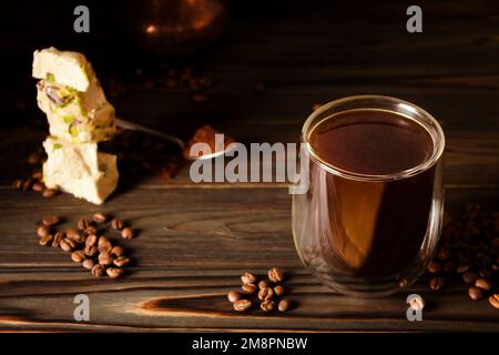 Frischer schwarzer Kaffee, der in der richtigen Enghalszeder gebrüht wird. Türkische Süßigkeiten. Türkische Halva mit Pistazien. Verstreute Kaffeebohnen Stockfoto