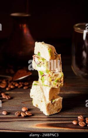 Organische Halova mit Pistazien auf einer Holzfläche. Traditionelle orientalische Süßigkeiten. Frischer Kaffee, Cezve aus Kupfer und verstreute Kaffeebohnen im Hintergrund Stockfoto
