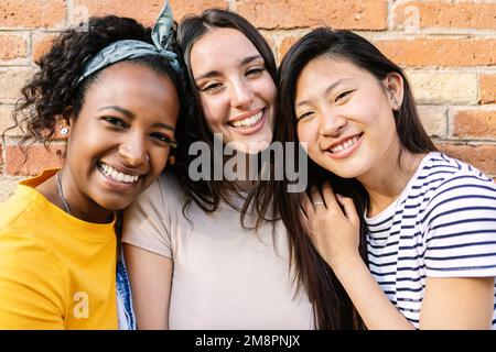 Lächelndes Porträt von drei jungen, vielfältigen Freundinnen, die draußen vor die Kamera schauen Stockfoto