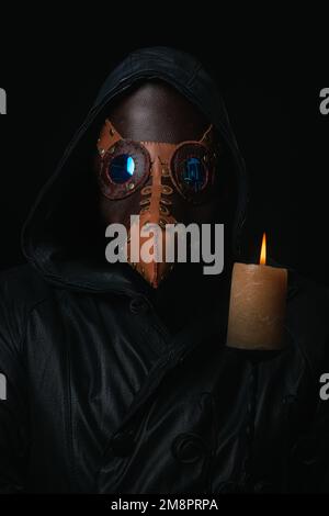 Pestdoktor mit Krähenartige Maske und Kerze isoliert auf schwarzem Hintergrund gruselig halloween historisch schreckliche Kostüm Konzept Epidemie Covid Pocken Stockfoto
