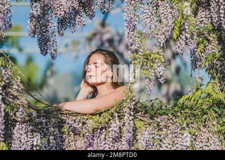 Nachdenklich glücklich reife Frau von chinesischen Glyzinien in lila Kleid umgeben Stockfoto