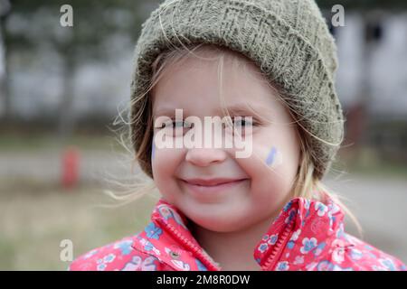 Porträt eines kleinen Mädchens in einem zerstörten Gebäude mit der ukrainischen Flagge im Gesicht. Flüchtlinge, Kriegskrise, humanitäres Katastrophenkonzept. Stockfoto