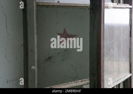 Roter Stern als Symbol des Kommunismus an der Wand in dem abgerissenen verlassenen Gebäude Stockfoto