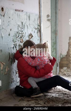 Mutter und Tochter in zerstörtem Gebäude. Krieg, Flüchtlinge, Kriegskrisenkonzept. Stockfoto