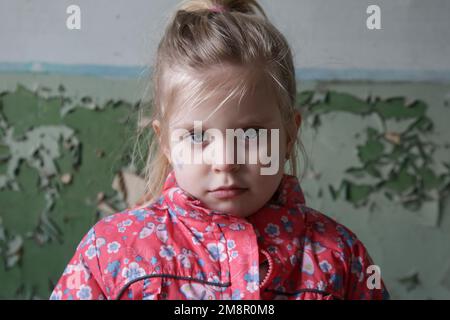 Porträt eines kleinen Mädchens in einem zerstörten Gebäude mit der ukrainischen Flagge im Gesicht. Flüchtlinge, Kriegskrise, humanitäres Katastrophenkonzept. Stockfoto