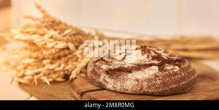 Banner mit Kopierbereich. Frisch gebackenes Roggenbrot auf einer hefefreien Vorspeise und einer Mischung aus Vollkorn, Roggen und Weizenmehl. Sie liegt auf einer Serviette, neben einer getrockneten Blume mit Getreide. Hochwertiges Foto Stockfoto