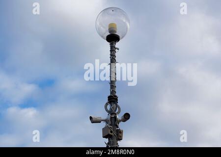 Zwei Überwachungskameras auf der Metalllampe für Straßenbeleuchtung im Freien auf blauem Himmelshintergrund. Sicherheit in der Stadt. Stockfoto