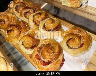 Die Linien von frisch gebackenen französischen und amerikanischen Zimtrollen, Croissants auf weißem Papier und Holzoberfläche Stockfoto