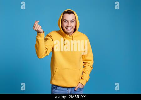 Junger Mann in gelbem Sweatshirt, der eine Liebesgeste zeigt Stockfoto