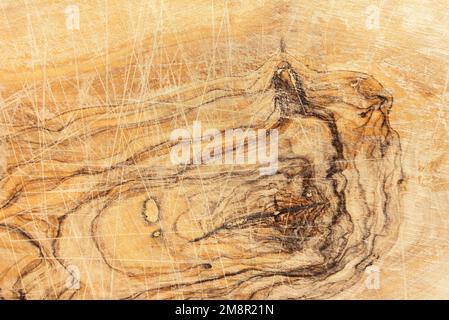 Detaillierte Nahaufnahme eines gebrauchten Schneidebretts aus Olivenholz mit Schnitten, Rillen und Patina der Verwendung Stockfoto