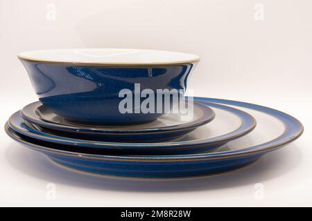 Eine blaue Schüssel und drei Größen Geschirrteller in Weiß mit blauen Rändern und goldenen Verzierungen Stockfoto