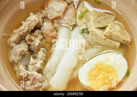 Große Reisnudeln, Wurstscheiben mit Kotelett und knusprigem Schweinefleisch, das weich gekochtes Ei in Suppe auf Schüssel serviert Stockfoto