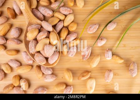 Erdnüsse in Holzlöffel auf Holzhintergrund. Ausgelaufene Gesalzene Erdnüsse Auf Holzhintergrund. Stockfoto